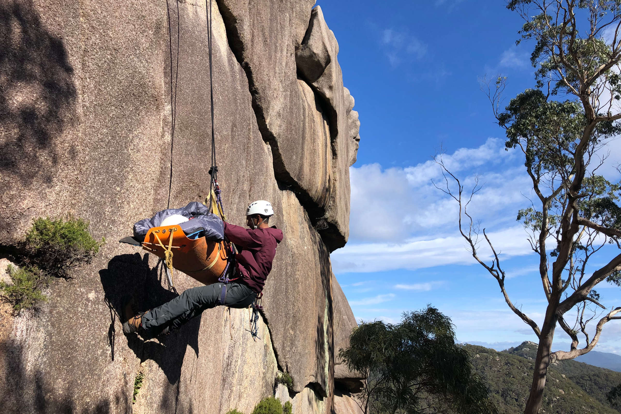 A man abseils down a rock face at Mount Cameron in Tasmania, supporting a patient in a stretcher in the front of his body. Photo: Clive Strauss.